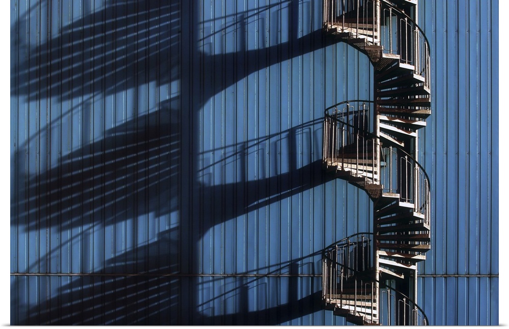 Architectural photograph of a spiral staircase casting shadows alongside a blue metal building.