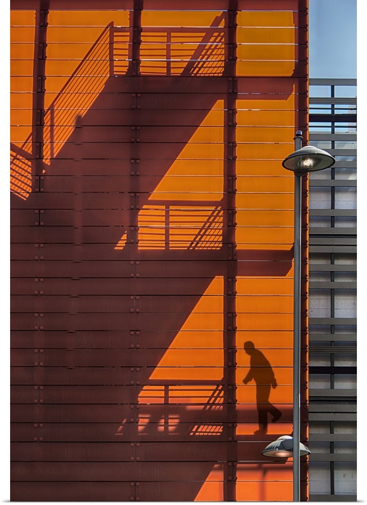 Shadow of a fire escape staircase and a person walking down cast onto the side of an orange building.