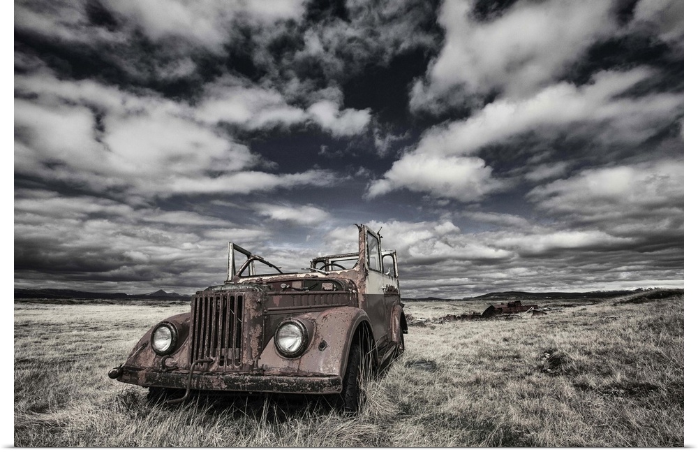A rusted, abandoned truck in a field in Iceland, under a cloudy sky.