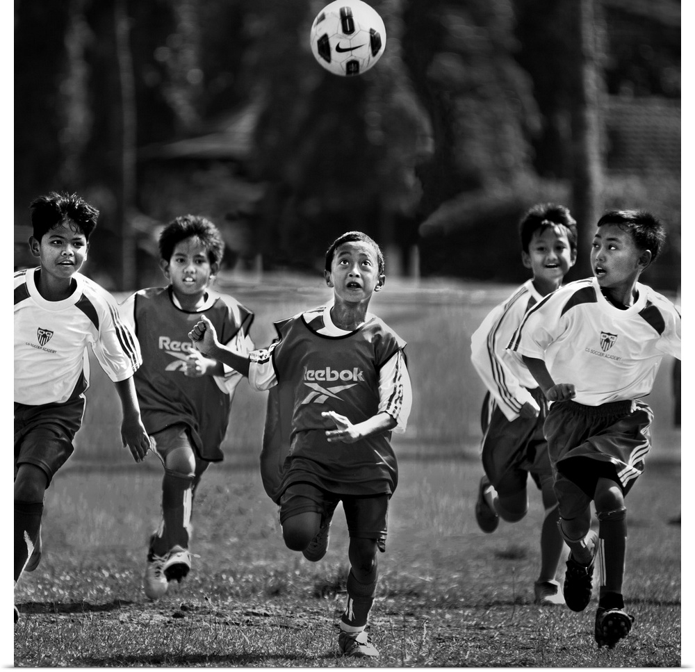 A group of young boys playing soccer in a field, with the ball in the air.