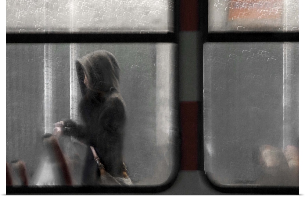 A women wearing a hood walking down the aisle of a train seen through the window.