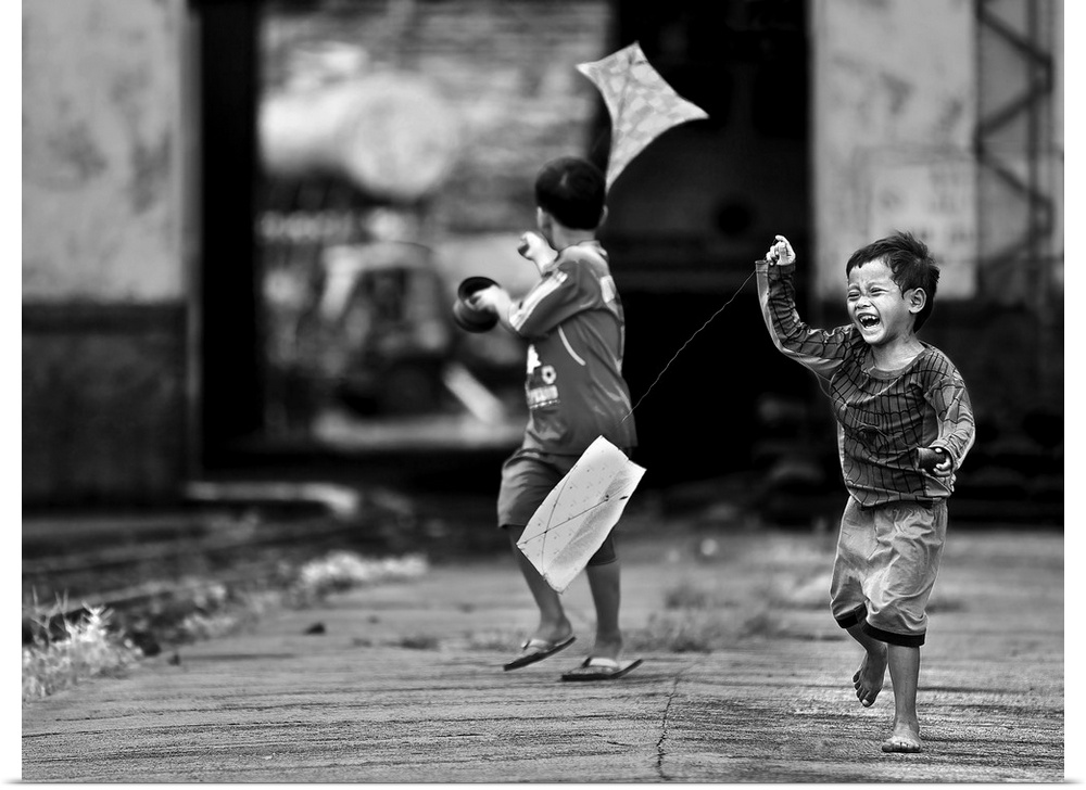 Two young boys pull kites behind them as the run down a street.
