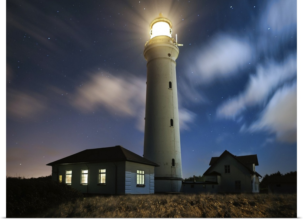 A lighthouse shining on the coast on a starry night.