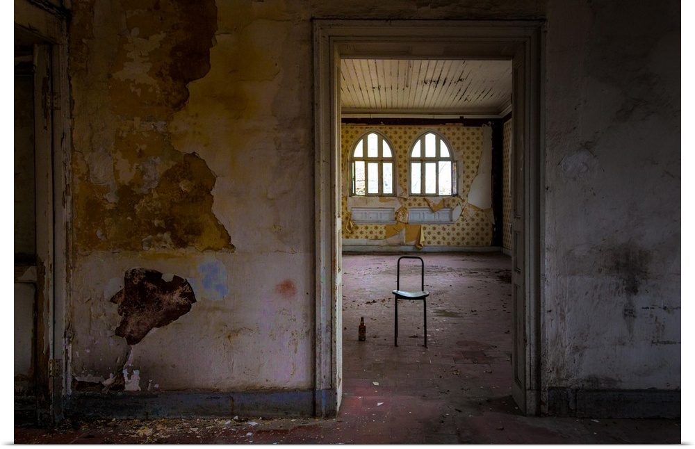 Interior photograph of an abandoned room with paint peeling from the walls, dirt on the floor, and a lone chair with a bot...