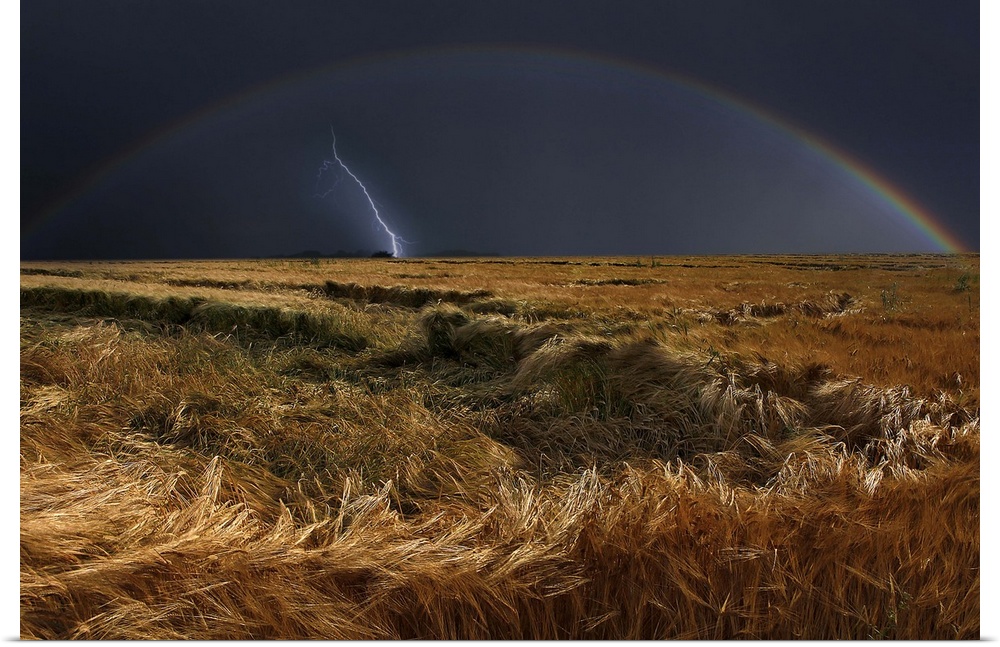 Field after storm with a rainbow in the dark sky and one final bolt of lightning.