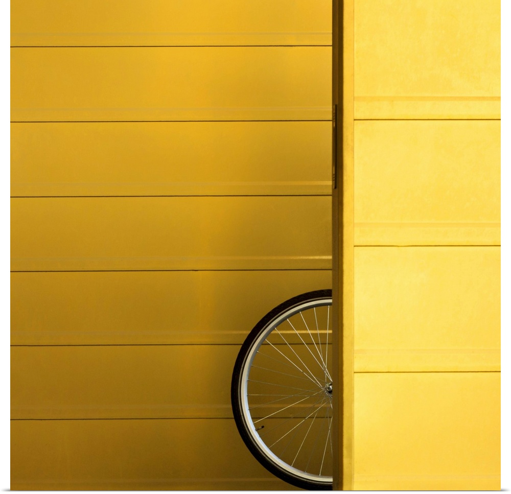 A bicycle wheel poking out from behind a yellow wall.