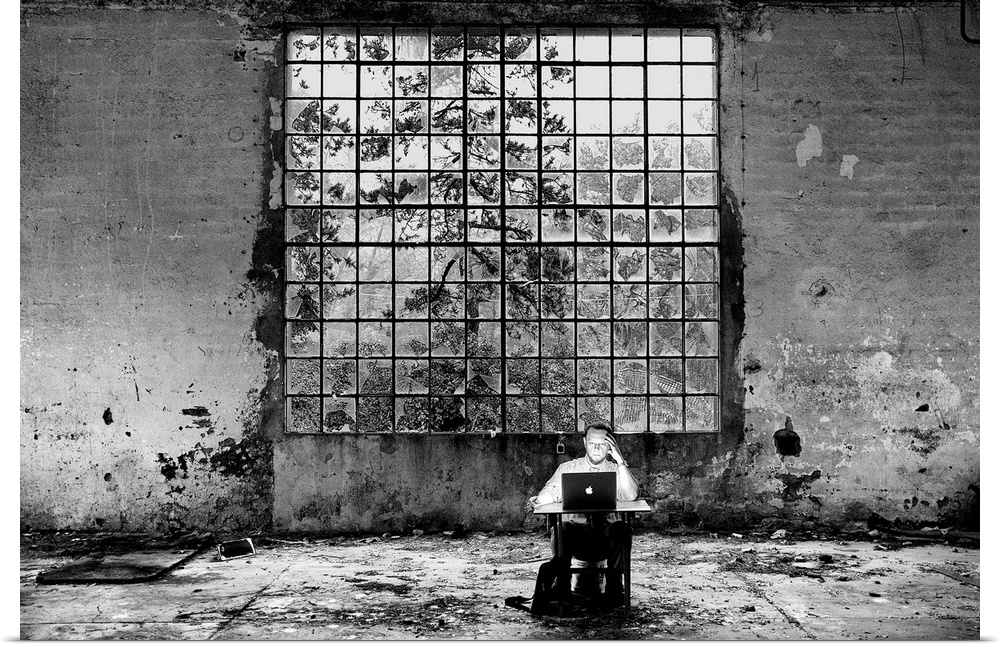 Conceptual photo of a man sitting at a desk in an abandoned building looking at a laptop.