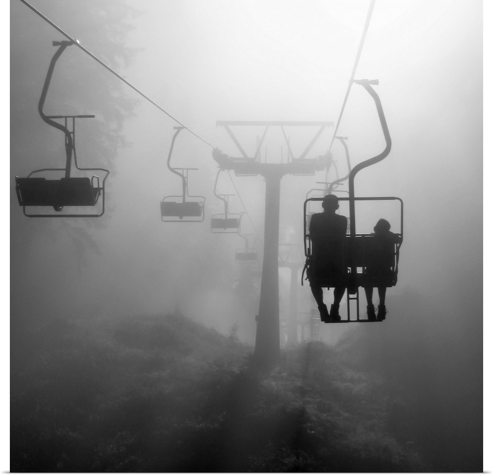 Two silhouetted people on a chairlift heading into the dense fog.