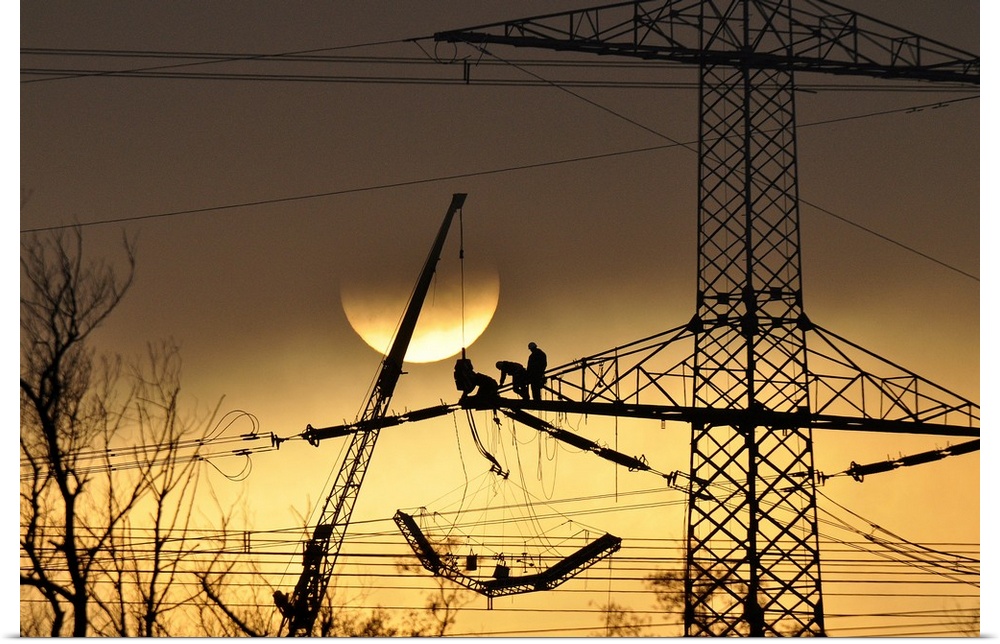 Silhouette of people working on a large electrical pylon with the sun setting in the background.