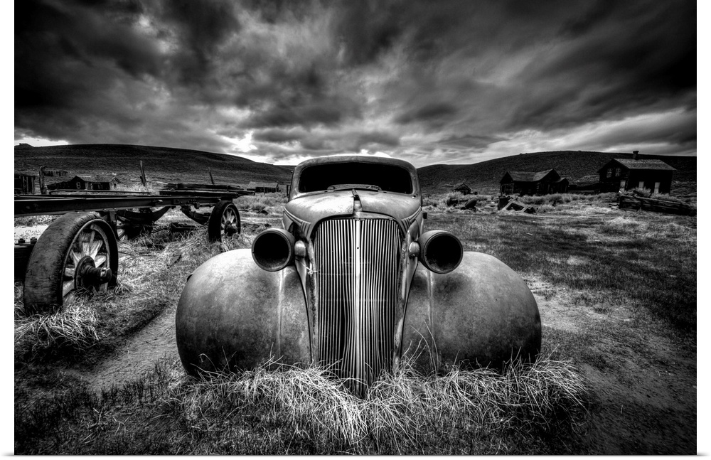 A black and white photograph of derelict vintage car sitting in a desert landscape.
