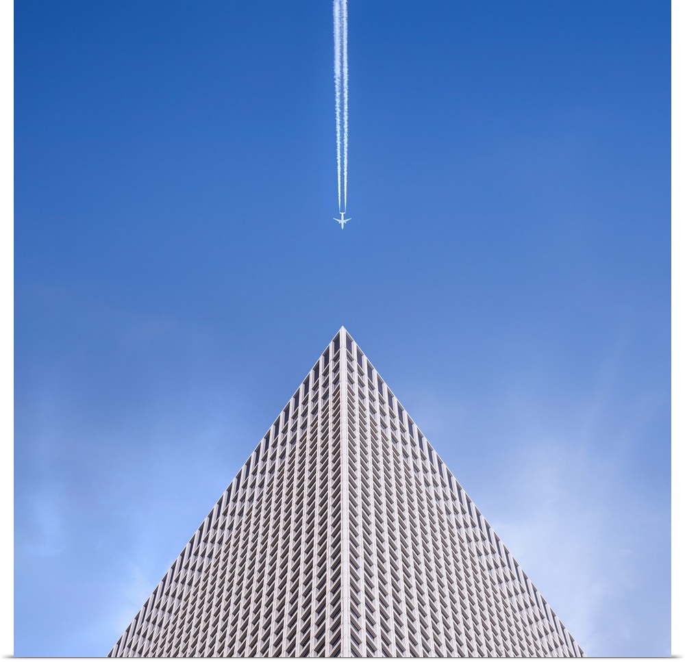 Looking up at the top of a skyscraper with an airplane leaving a vapor trail behind him.