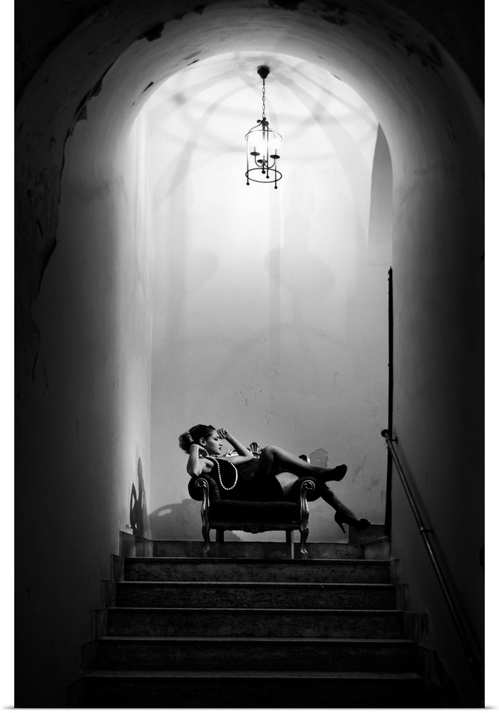 A black and white photograph of a woman in black dress sitting in chair at the top of a staircase.