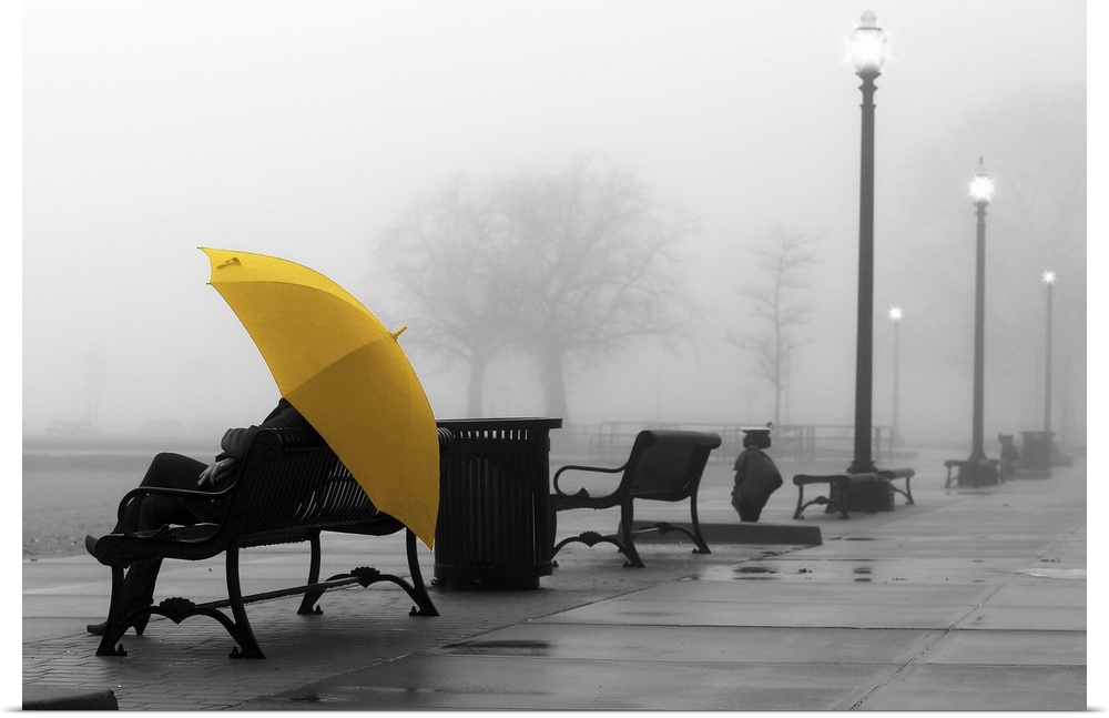 A black and white photograph of a person with a colorized yellow umbrella sitting on a bench on a foggy day.