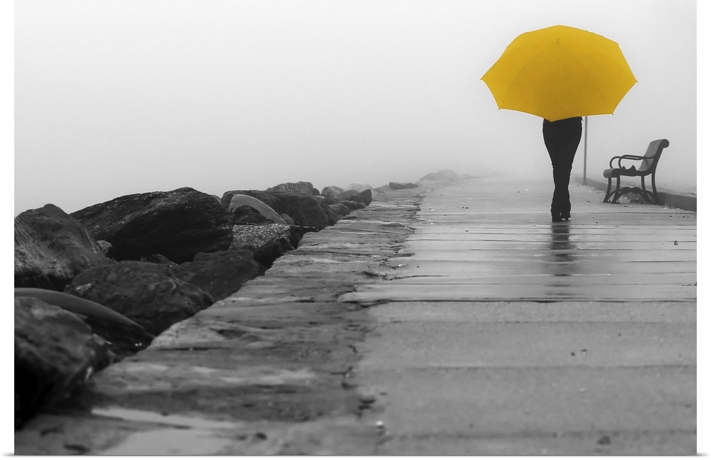 A black and white photograph of a person with a colorized yellow umbrella sitting on a bench on a foggy day.