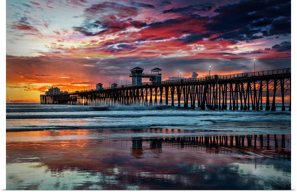 Summer sunset at the Oceanside Pier. The Oceanside Pier is silhouetted as sunset turns the reflected clouds from yellow to...