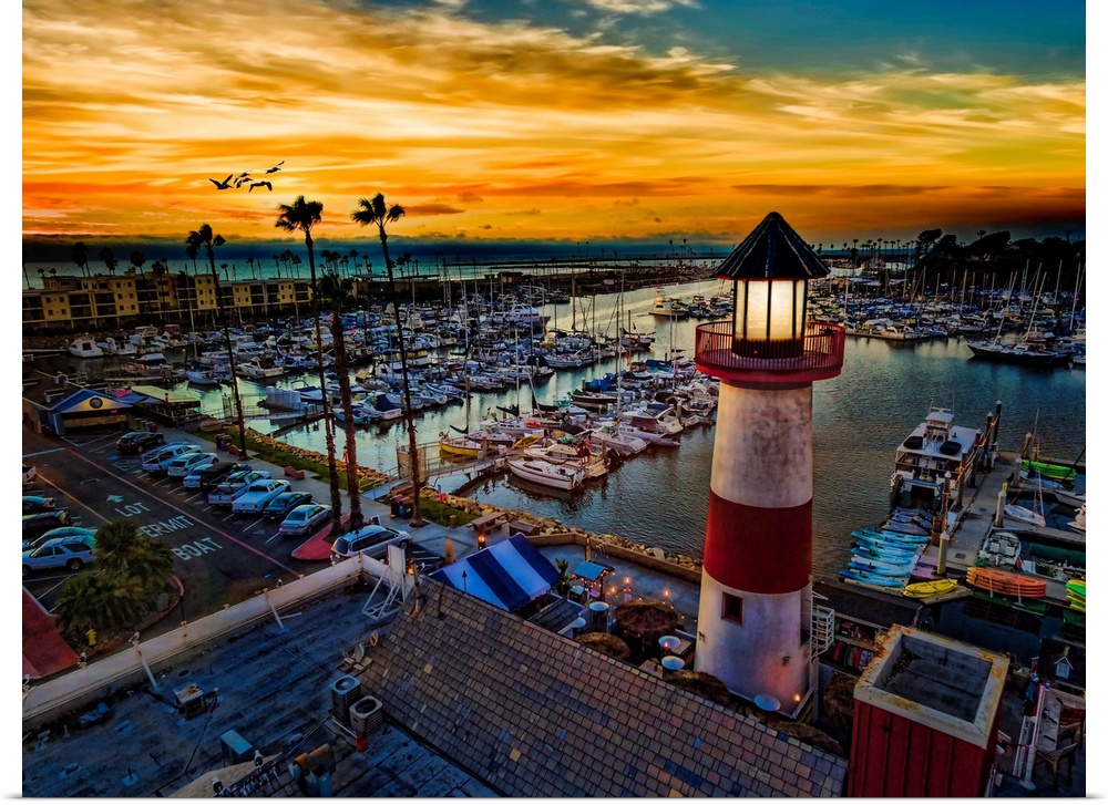 Pelicans glide over the Oceanside Harbor and the little lighthouse glows. Colorful sunset in Oceanside, California, USA.