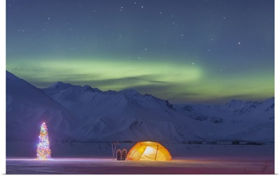 A tent and decorated Christmas tree glow under the Northern Lights