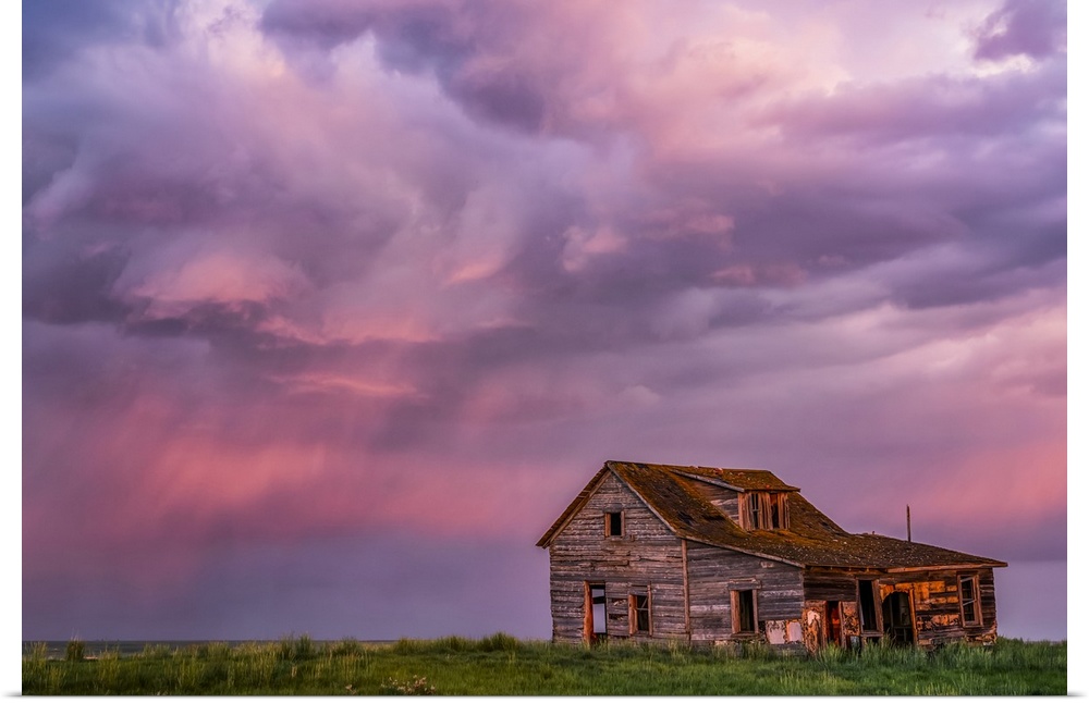 Abandoned barn on farmland with storm clouds glowing pink; Val Marie, Saskatchewan, Canada