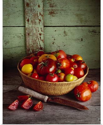 Basket of heirloom tomatoes of various varieties with a slicing knife and sliced tomato