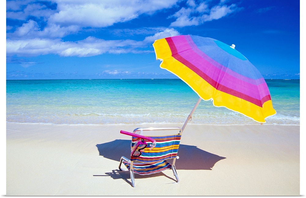 A large photograph of a colorful beach chair and umbrella sitting solely on the sand close to the clear ocean water.