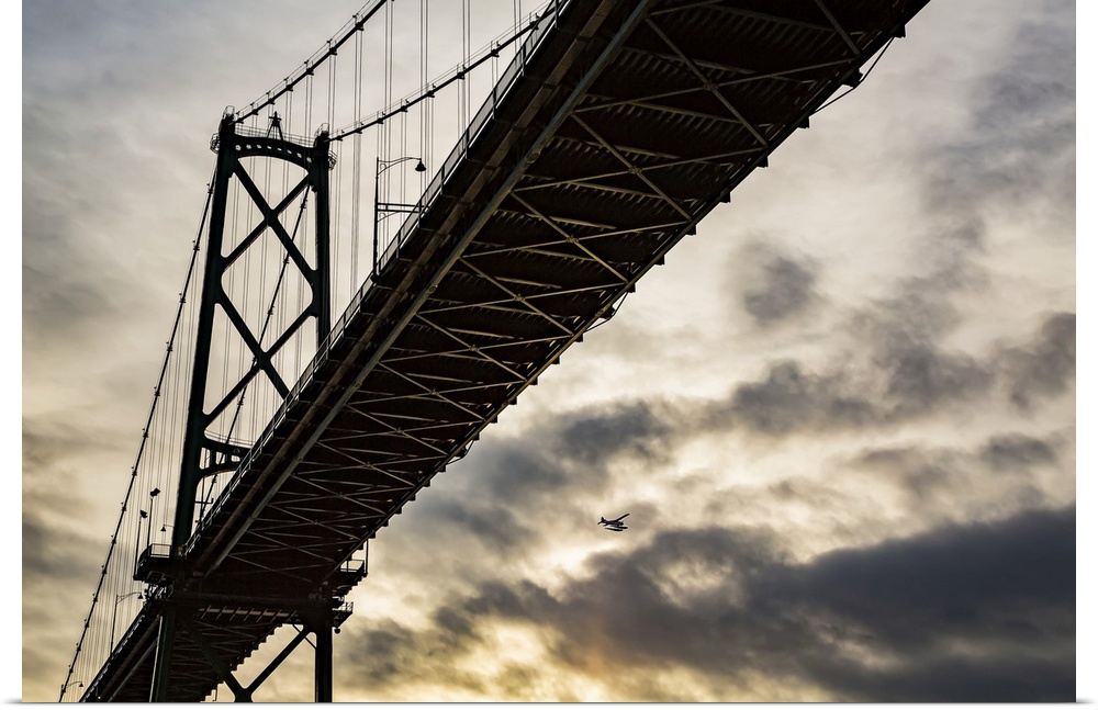 Low angle view of a bridge at sunset with an airplane flying in the distance; Vancouver, British Columbia, Canada