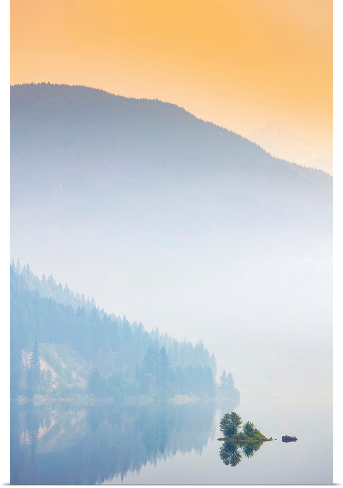 Dense fog over a lake and mountain with a glowing orange sky at sunrise; British Columbia, Canada
