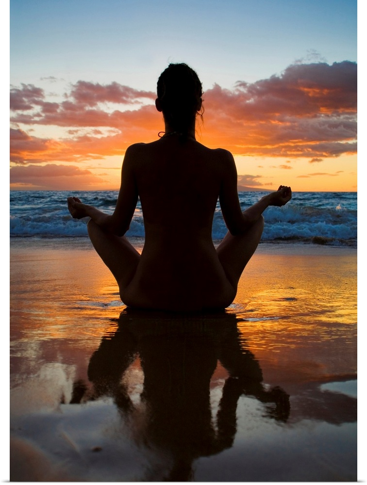 Woman meditating and doing yoga on the wet sand as the surf breaks in front of her and the sun setting creating a silhouet...