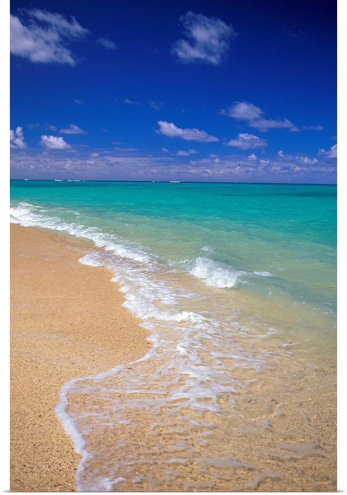 Shallow waters recede from the sandy coastline of a tropical beach, the clear sea stretching out into the distance.