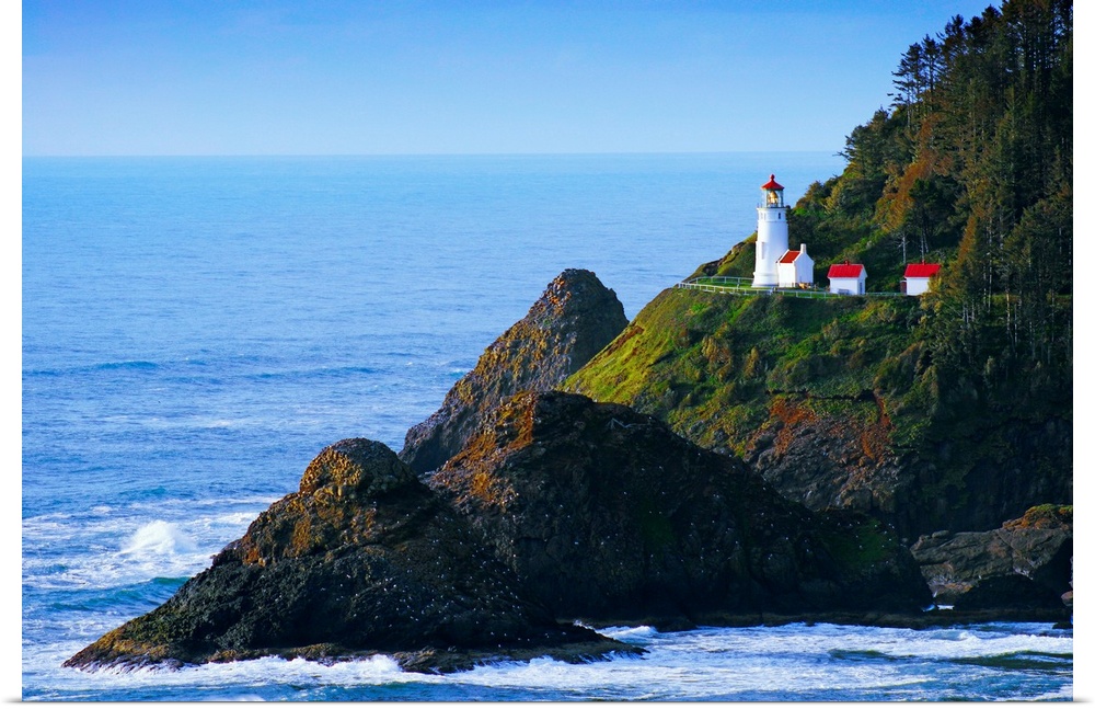 A lighthouse stands on the edge of a cliff that is surrounded by large rock formations in the Pacific ocean.