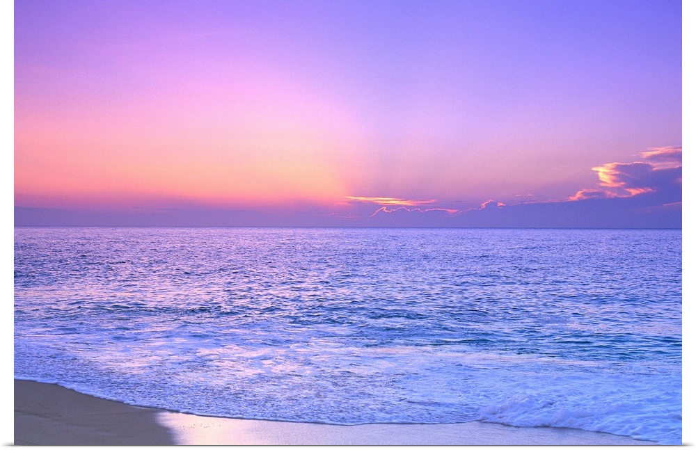 A breathtaking photograph of a sunset over the vast ocean giving the overall picture a soft colored hue.