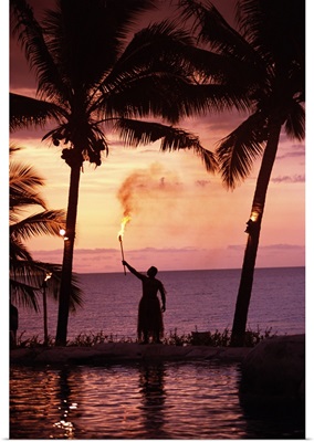 Native In A Grass Skirt Holding A Flaming Torch By Coast At Sunset
