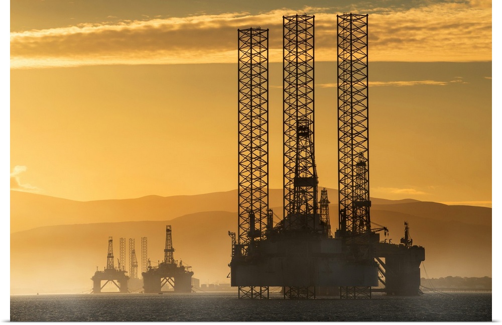 Oil drilling rigs out in the ocean with a view of the coastline and golden sunset; Cromarty, Invergordon, Scotland
