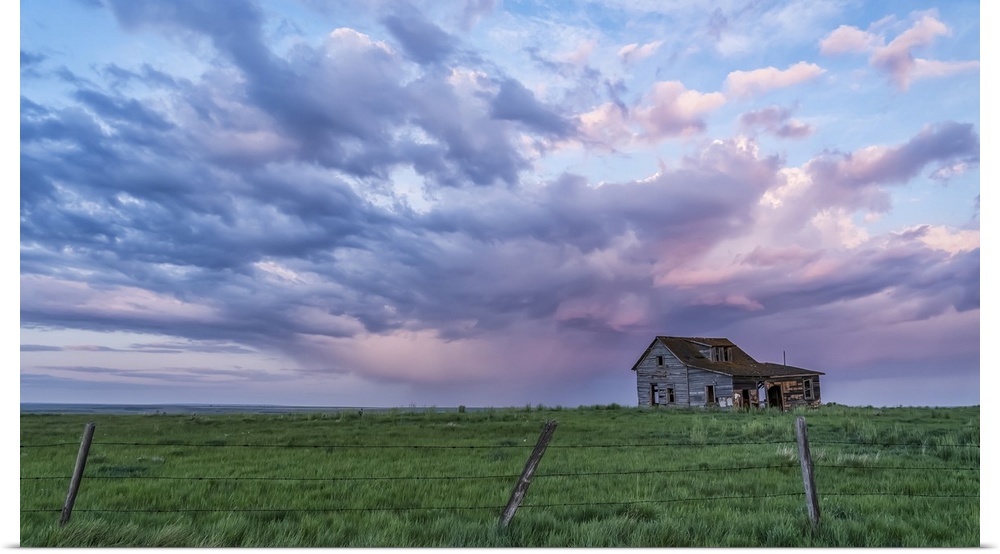 Old farmstead on the prairies under glowing storm clouds at sunset; Val Marie, Alberta, Canada