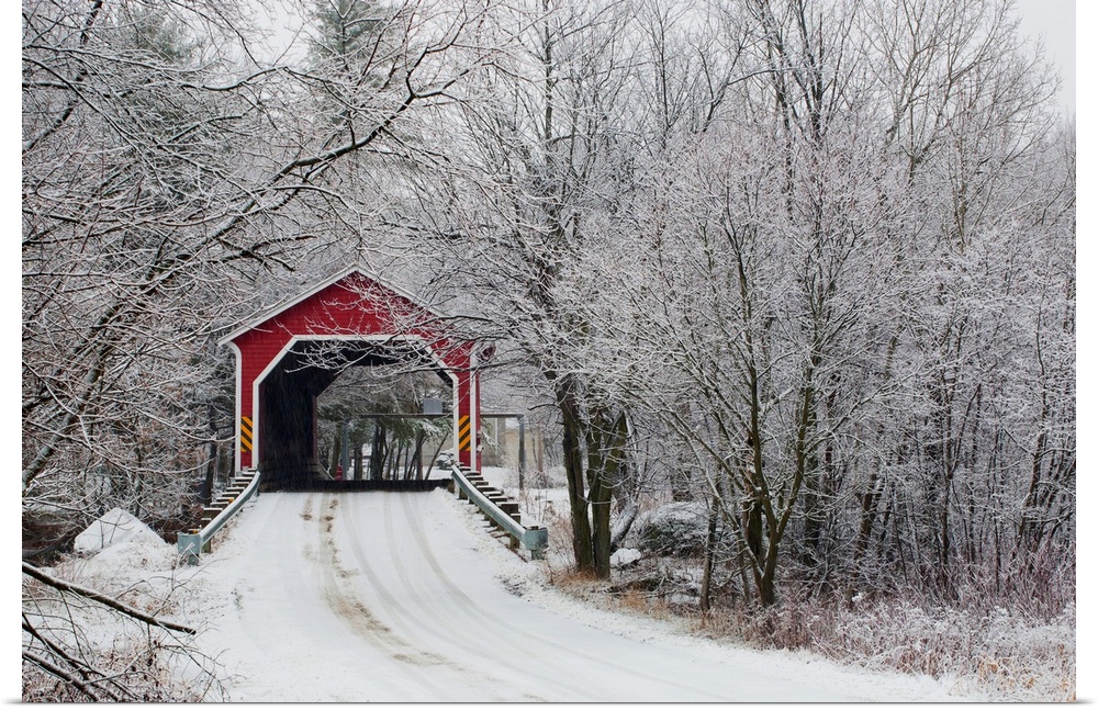 Snow covered trees surround a road that leads up to a covered bridge.