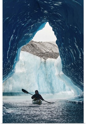 Sea Kayaker paddles through an ice cave amongst giant icebergs near Bear Glacier