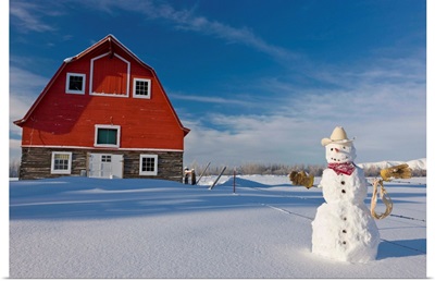 Snowman dressed up as a cowboy standing in front of a vintage red barn