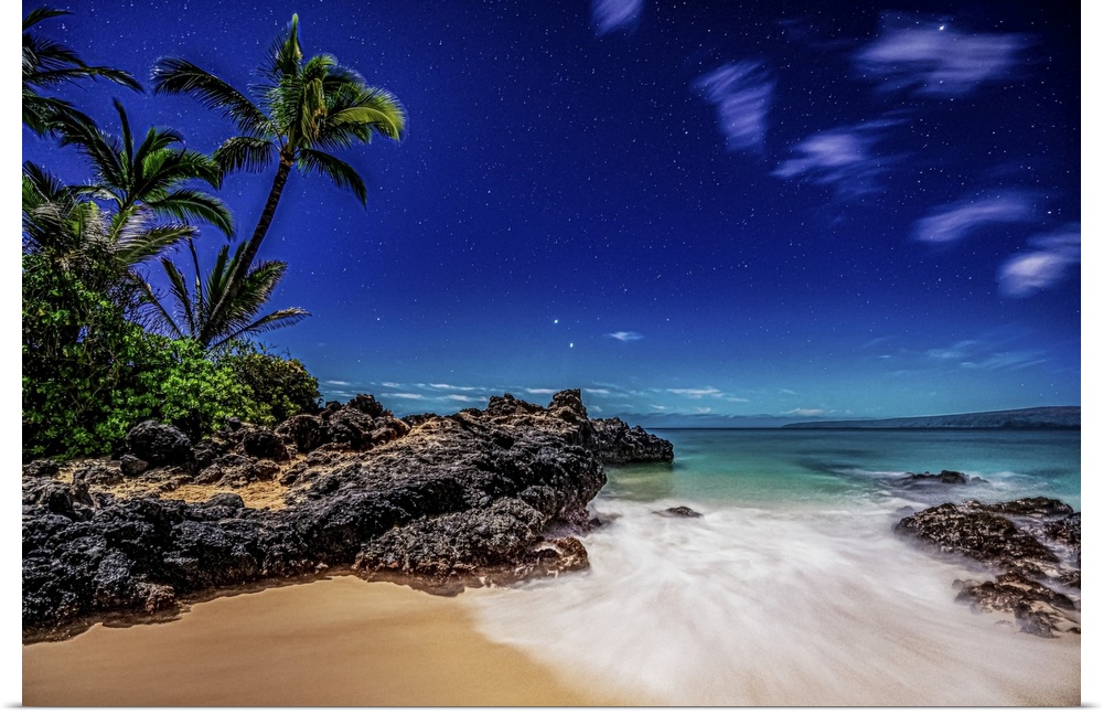 Starry skies viewed from a beach with palm trees and surf rolling into golden sand at Makena cove on the island of Maui, H...
