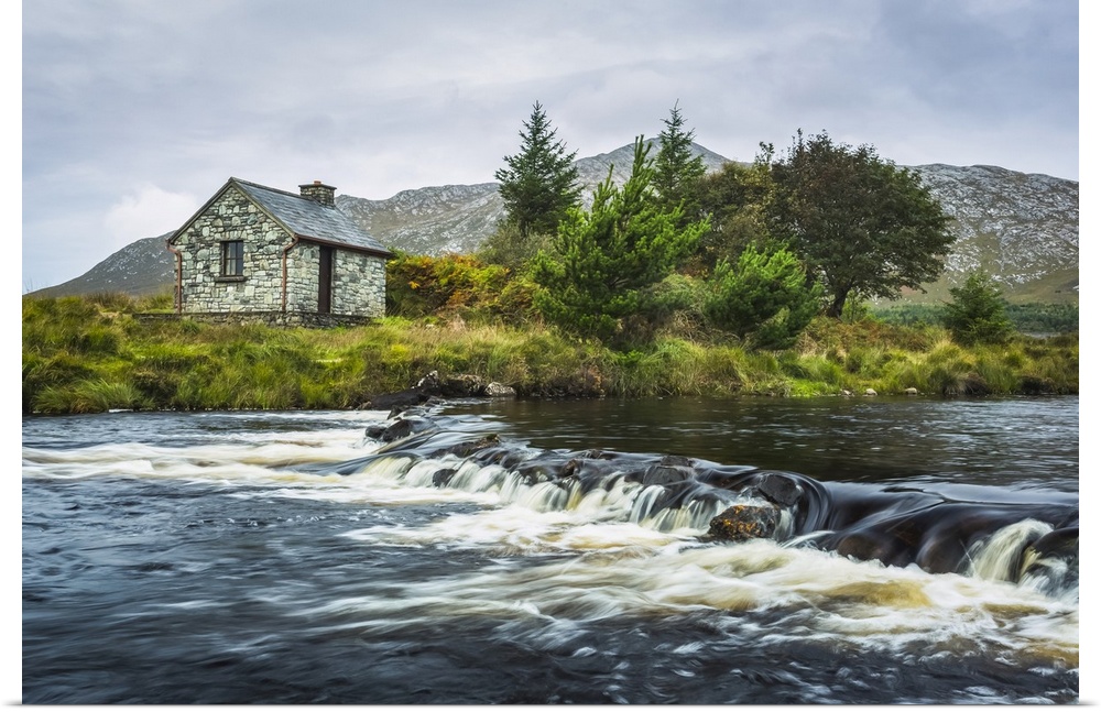 Small stone fisherman's hut on the banks of a small river with mountains in the background on a cloudy day; Connemara, Cou...