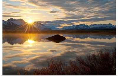 Sun rises over the Chugach Mountains with a pond and beaver lodge in the foreground