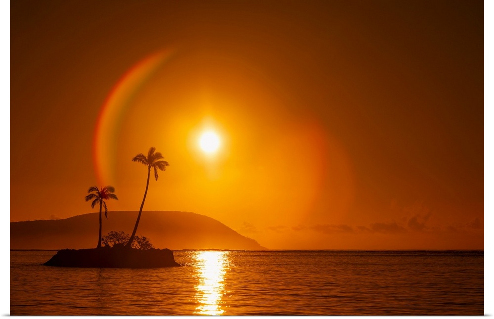 Sunrise at Kahala Beach, Waialae Beach Park, with a flare around the sun in a glowing red sky reflected in the tranquil wa...