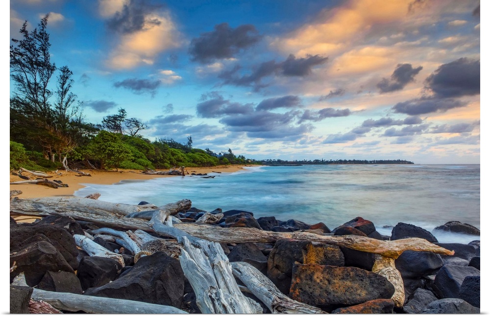 Sunrise over Lydgate beach and ocean with rocks and driftwood in the foreground and the coastline in the distance; Kapaa, ...