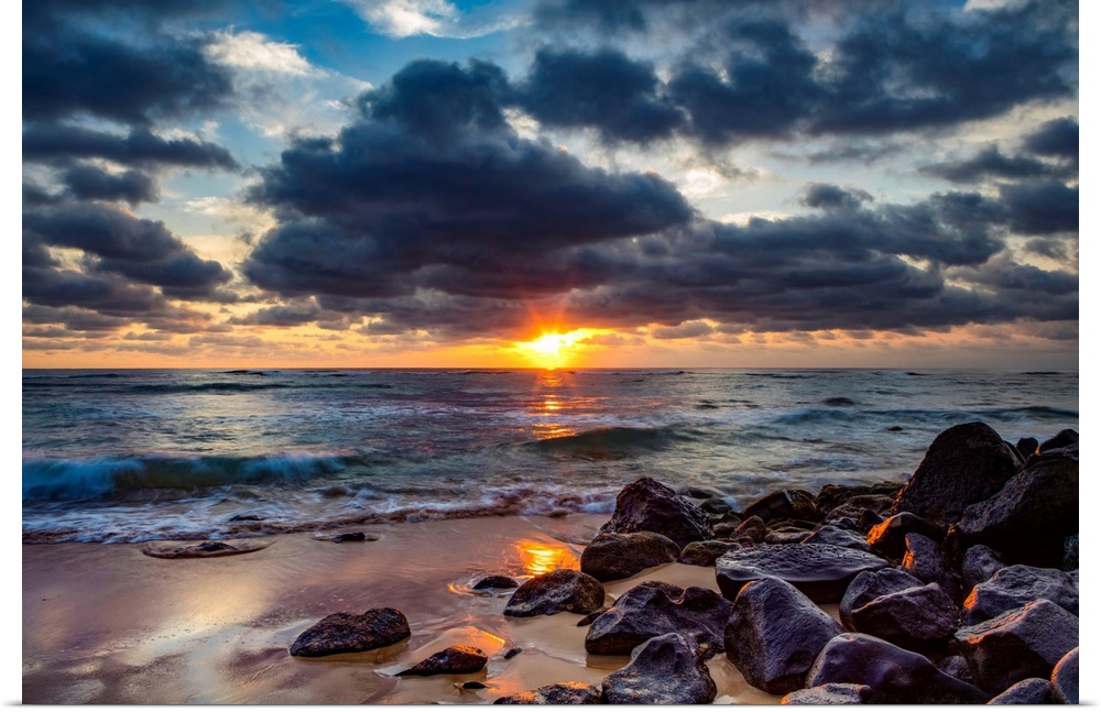 Sunrise over the Pacific Ocean from the rocks on the shore of Lydgate beach and dark clouds overhead. Kapaa, Kauai, Hawaii...