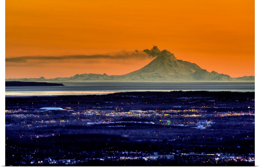Ash billows out of an active volcano which looms over a city in the evening in the Aleutian mountain range.
