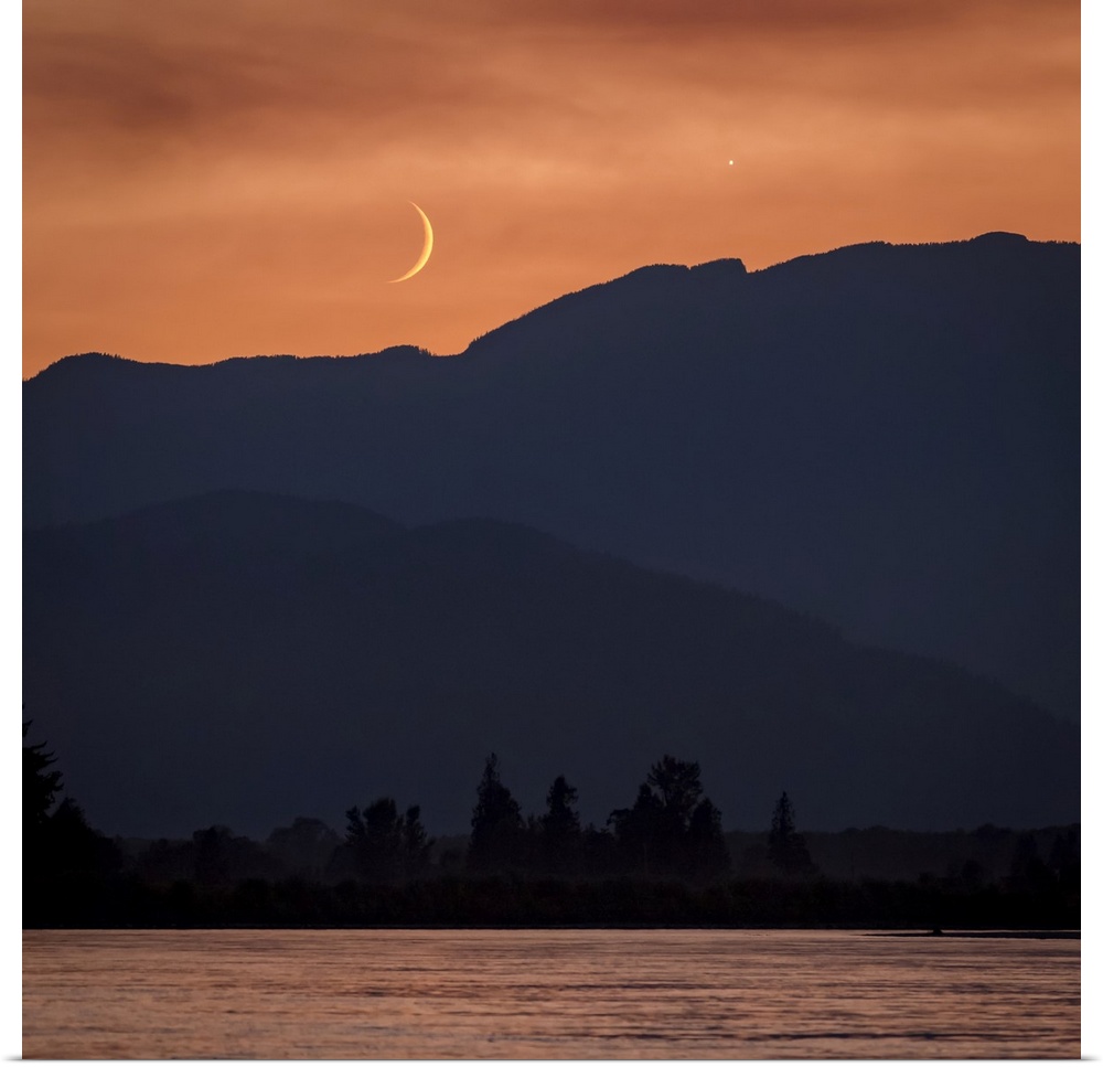 The moon and Venus in an orange sky over the silhouetted mountains, Fraser Valley; Vancouver, British Columbia, Canada