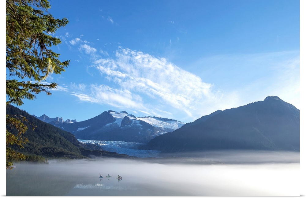 Three Kayakers paddle the shoreline of Mendenhall Lake as morning fog clears, Tongass National Forest, Juneau, Alaska.