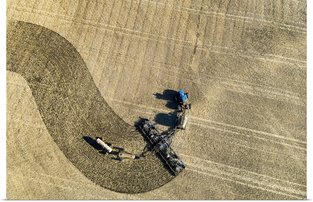 Aerial view of a tractor pulling an air seeder, seeding a field; Beiseker, Alberta, Canada
