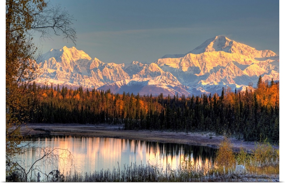 Serene landscape at dawn of two snow-covered mountains near a pine forest at the edge of a small pond in Alaska.