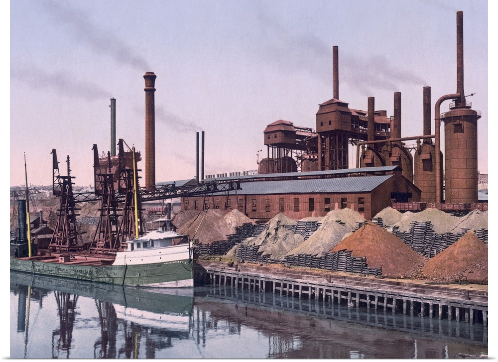Vintage color photo of an American Steel factory on the banks of a river with tall smoke stacks and piles of minerals.