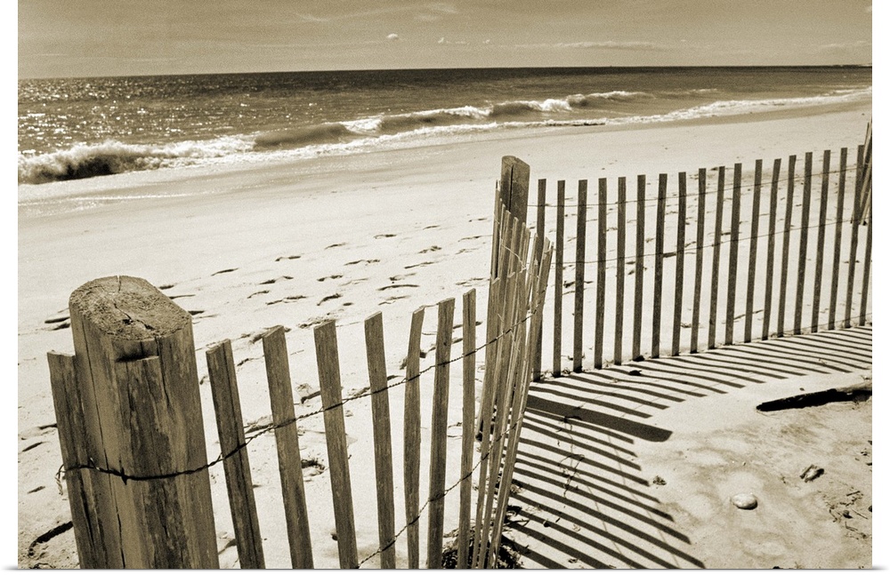 Sepia toned photograph of a sand dune fence casting long shadows on a sandy beach.