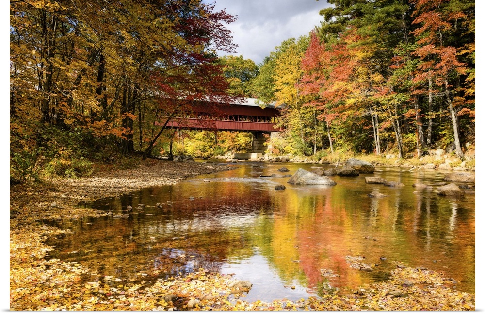 A photograph of a covered bridge spanning a stream in a forest in autumn foliage.
